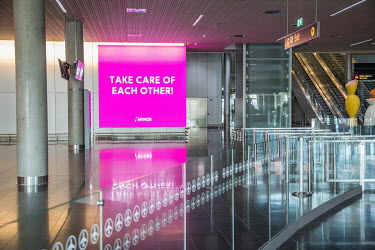 A huge digital display panel with the message 'Take care of each other' at an almost deserted Gardermoen Airport.  Restrictions on public gatherings and travel have grounded most aeroplanes, and stopp...