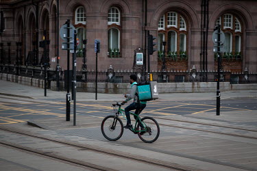 A Deliveroo cyclist rides across tram tracks in St Peter's Square while delivering food take-aways in an almost empty Manchester city centre on a Saturday evening during the coronavirus lockdown.