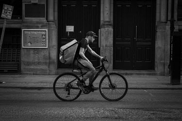 A Deliveroo delivery cyclist delivering take-aways in an almost empty Manchester city centre on a Saturday evening during the coronavirus lockdown.