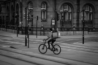 A Deliveroo cyclist rides across tram tracks in St Peter's Square while delivering food take-aways in an almost empty Manchester city centre on a Saturday evening during the coronavirus lockdown.
