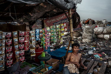 A rubbish picker takes a break from searching for recyclable plastic and other items at the Bantar Gabang landfill, to rest beside a stall selling snacks to recyclers and others at the site.