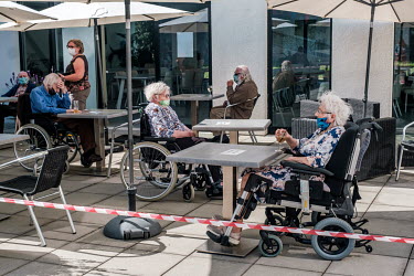 Residents at the De Muze nursing home sit outside on a terrace where, as long as they wear face masks and stcik to social distancing rules, they can order drinks and enjoy the sunshine.
