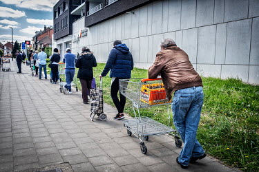 A queue outside a supermarket includes a man returning a crate of empty beer bottles.