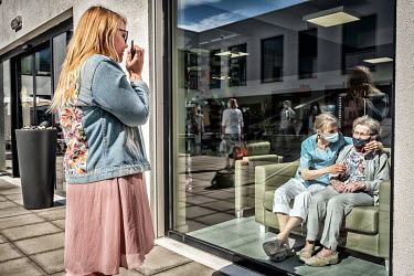 A woman, visiting a relative who is a resident at the De Muze nursing home, looks at her relative through a large window while communicating via a walkie-talkie.