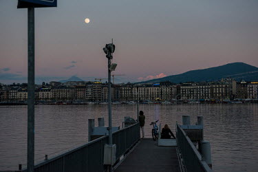 People on a jetty on Lake Geneva with Mont Blanc and a full moon beyond them. It is week two of stage one of a three stage de-confinement process, in the eighth week after the start of the coronavirus...