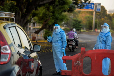 Police officers dressed in a hazmat suit prepare to examine the credentials of drivers at a checkpoint to see if they are travelling legitimately.