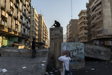 A young man sat atop broken blast walls put in place to stop protesters from occupying land in the city centre.  Since the beginning of October 2019 huge anti-government protests have shaken the count...