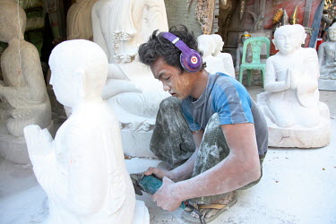 A boy making and polishing a Buddha statue, working without any facial protection, at a factory near the Mahamuni Pagoda.