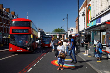 Pedestrians waiting at a bus stop use a 'Streetspace' pavement extension on Brixton Road.