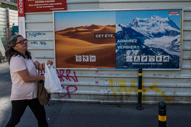A woman passes an billboard advertising holidays at home in Switzerland, due to the pandemic, for mountain resort Verbier. The poster states 'This Summer, come and see Verbier' and exploits icons simi...