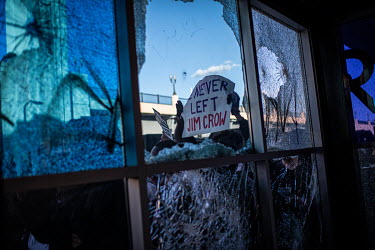A protestor, seen through a broken window, holds a sign that reads: 'We Never Left Jim Crow' during protests and unrest that resulted from the killing by the police of George Floyd, an unarmed African...