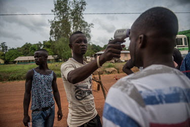 Youths use a thermometer to screen people for Ebola at the entrance to their village near Makeni.