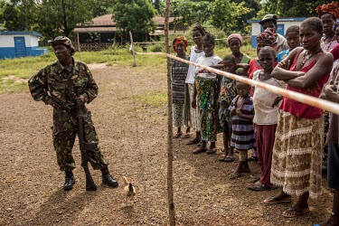 Residents of a village hit by Ebola stand behind a quarantine line guarded by a soldier.
