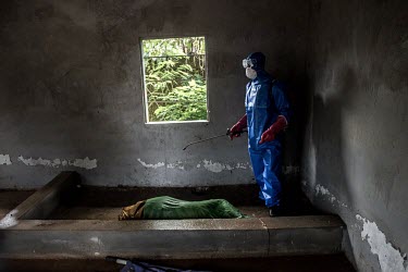 An Ebola burial team disinfect the body of an woman, suspected to have died from Ebola, before placing her inside a body bag at a health center outside Makeni.