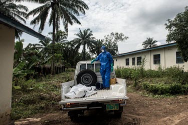 A burial worker stands in the back of a pickup truck next to the body of an woman suspected to have died from Ebola.