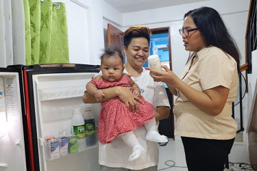 Mylene Garcia Seloterio (R), holding a container of her expressed breastmilk, as she gives feeding information to her baby's carer before heading to work. Seloterio is a teacher and has just return to...