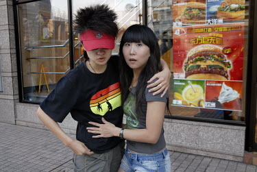 A young couple in front of a branch of a McDonald's restaurant.