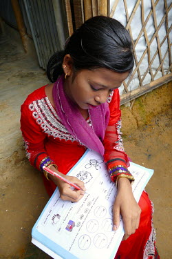 Rohingya refugee Showkat Ara (15) fills out answers in a children's text book. Although she studied up to grade six she is not in currently school but she would like to return. She lives with both par...