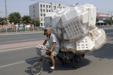A man carries a load of polystyrene to a dealer on a bicycle-cart.