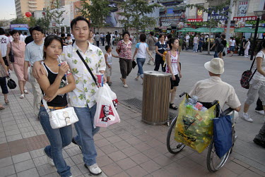 A disabled man collects empty plastic bottles and tins, to sell to recyclers, from a crowded Wangfujing Street.