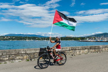 A man cycling along Geneva waterfront carrying a Palestinian flag.