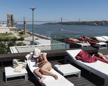Women sunbathing on the rooftop terrace at the Altis Belem Hotel and Spa. In the background is the Ponte 25 de Abril (25th of April Bridge), a suspension bridge connecting the city of Lisbon, to the m...