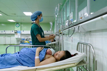 A nurse checks the medication as Huynh Thi My Hanh holds her new born baby that has just been delivered by c-section at the Da Nang hospital for women and children.