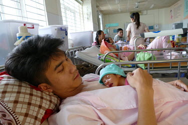 Nguyen Duy Minh lies on a hospital bed with his new born baby lying on his chest at the Da Nang hospital for women and children.