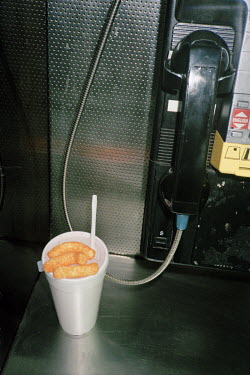 Cheese snacks and a styrofoam cup discarded in a public phone booth.