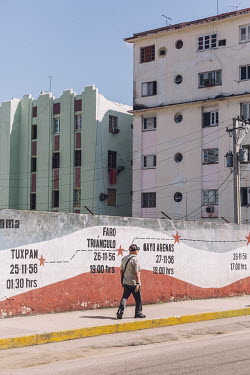 A man walks down a street passing a Cuban revolution timeline mural.