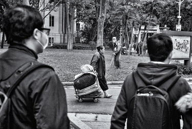 A homeless woman pulls her belongings on a trolly through Taipei's 228 Peace Park as commuters head to their work in nearby offices and a man cuts the grass.