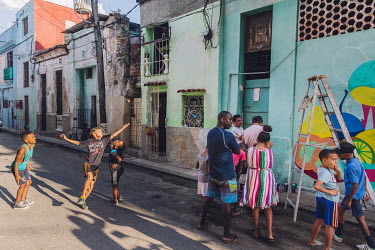 Local residents gather to watch a street artist painting a mural while children play handball in the San Isidro neighbourhood.