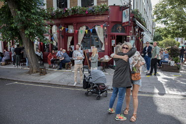Two women embrace as people socialise in the street outside a pub in Notting Hill after easing of coronavirus lockdown restrictions enabled some businesses to open subject to staff and customers maint...