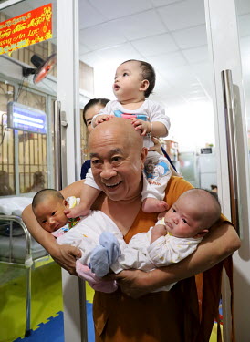 A monk holding new born babies in a hospital's maternity ward.
