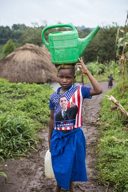 A girl wearing a Barack Obama t-shirt and carrying a watering can on her head, on her way to collect water at a public tap.