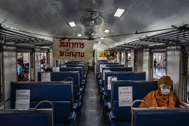 A Thai Buddhist monk sits on a train waiting to depart from Bangkok Railway Station. The seat beside him has a sign in Thai and English which reads: 'Do Not Sit', as rail authorities encourage social...