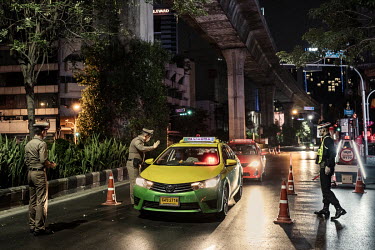 Police officers, wearing protective face masks, stop a taxi at a checkpoint on Sukhumvit, one of Bangkok's busiest streets, as Thai authorities impose a nationwide night time curfew from Friday 3 Apri...