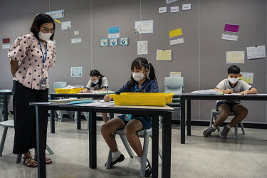 A teacher looks at one of her students in a classroom at the Bangkok Patana School where everyone wears face masks and practices social distancing protocols.