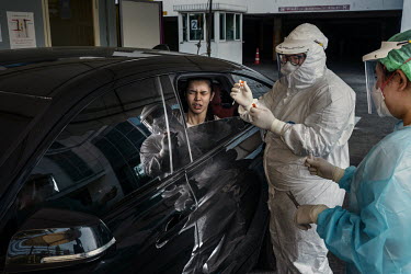 A woman grimmaces as she reacts after being tested for COVID-19 at a drive through testing centre outside a hospital.
