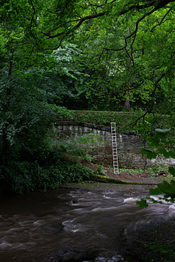 A ladder leans against a wall in a private community park beside the Water of Leith river near Stockbridge.  Hedges offer increased privacy, isolating the homeowner and emphasising the division of pub...