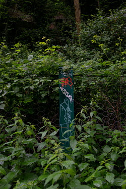 Graffiti covers a metal fence post errected to protect pedestrians against rock falls beside the Water of Leith river near Stockbridge.  Hedges offer increased privacy, isolating the homeowner and emp...