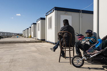 Two migrants sitting in front of their 'container house' in the 'Tent Village Open Centre'. A container house accomodates up to two families or eight individuals. Most residents are Africans, predomin...