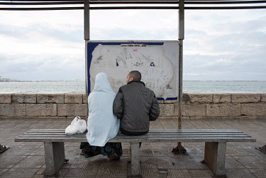 A couple sit on a bench on the Corniche beside the Mediterranean Sea.