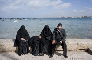 A man sitting with three women wearing niqabs beside the Mediterranean Sea.
