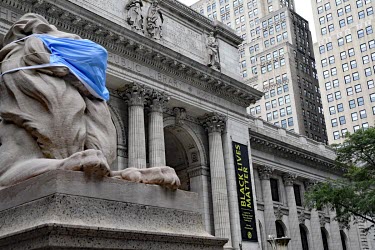 A Black Lives Matter reading list advertised on a banner at a Public Library where a statue of a lion at the entrance has had its face covered by a giant 'face mask'.