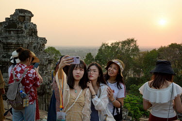 Chinese tourists take a group selfie photograph at sunset during a visit to the Phnom Bakheng temple in the Angkor Wat temple complex.