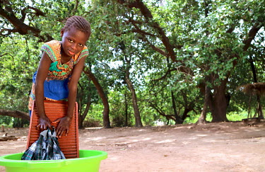 A girl washes clothes in a plastic basin.