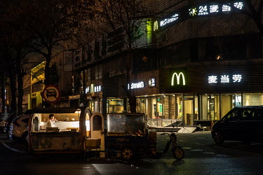 A mobile snack van parked on a street corner outside of a 24hr McDonald's fast food restaurant.