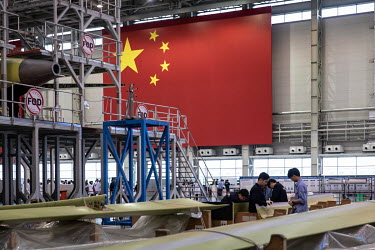Technicians examine the wing flaps of a Commercial Aircraft Corp. of China Ltd. (Comac) C919 as it is assembled beside a large Chinese national flag hanging at the Comac Shanghai Research and Developm...