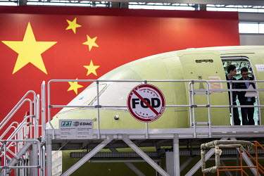 Technicians exit a Commercial Aircraft Corp. of China Ltd. (Comac) C919 as it is assembled beside a large Chinese national flag hanging at the Comac Shanghai Research and Development Center.